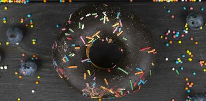 Beautiful sweet food. Colorful chocolate donut with colored sprinkles on a wooden background. photo
