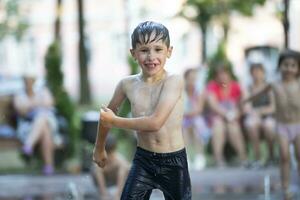 un pequeño chico disfruta el frío aguas de un fuente durante el calor ola. foto