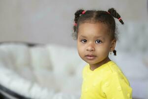 pequeño africano americano niña en un amarillo vestir mira a el cámara. foto