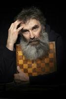 retrato de un mayor hombre con un gris barba con un tablero de ajedrez. foto