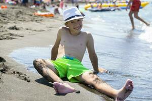 The boy sits on the seashore on black sand. photo