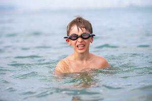 A boy in swimming goggles swims in the sea. photo