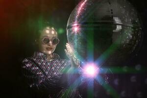 A beautiful girl in stylish glasses is spinning a sparkling disco ball. photo