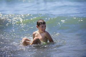 Happy boy swims in the sea, plays with the waves. Child on vacation at the seaside. photo