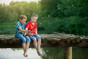 Two boy friends are sitting on a wooden bridge and fishing. Children on a fishing trip. photo