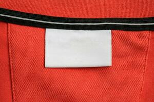 Blank white laundry care clothes label on orange shirt fabric texture background photo