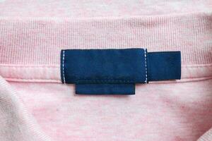 Blank blue laundry care clothes label on pink shirt fabric texture background photo