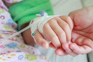 madre participación niño mano con salina iv solución en hospital foto