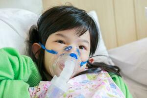 Sick little asian girl inhalation with nebulizer for respiratory treatment photo