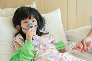 Sick little asian girl inhalation with nebulizer for respiratory treatment photo