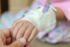 Mother holding child hand with saline IV solution in hospital photo