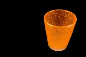 a glass of orange liquid sitting on a black surface photo