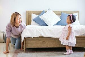 Mother is playing peek a boo or hide and seek with her little baby toddler in the bedroom while the girl is laughing in happiness for good parenting and healthy raising kid photo