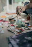 Selective focus. Oil painting techniques. Close up view of male artist holding brush mixing oil paints in colorful plastic palette on floor. photo