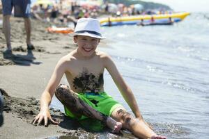 el chico se sienta en el costa manchado en negro magnético arena. médico playa. foto