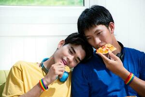 Portrait of two young asian gay couples sitting on sofa, spending their free time and watching tv at home together, concept for lifestyle of LGBT people around the world. photo