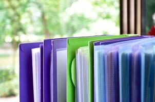 Back view of various plastic file folders for storing important documents in a file box for neatness and easy finding places near transparent glass window, blurred edited background. photo