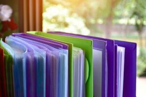 Back view of various plastic file folders for storing important documents in a file box for neatness and easy finding places near transparent glass window, blurred edited background. photo