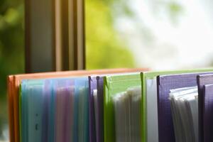 Back view of various plastic file folders for storing important documents in a file box for neatness and easy finding places near transparent glass window, blurred edited background. photo