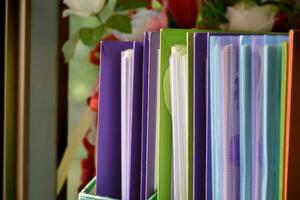 Back view of various plastic file folders for storing important documents in a file box for neatness and easy finding places near transparent glass window, blurred edited background. photo