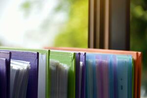 Back view of various plastic file folders for storing important documents in a file box for neatness and easy finding places near transparent glass window, blurred edited background. photo