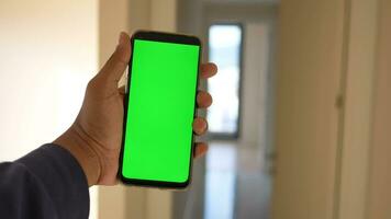 närbild hand använder sig av telefon som visar grön skärm i tömma rum video