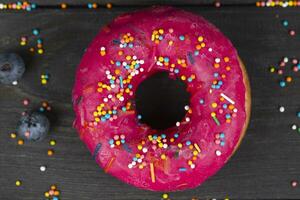 Beautiful sweet food. Colorful pink donut with colored sprinkles on a wooden background. photo