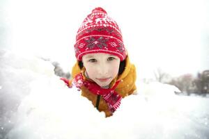 gracioso pequeño chico en vistoso ropa jugando al aire libre durante un nevada. activo Días festivos con niños en invierno en frío Nevado días. contento niño es teniendo divertido y jugando en invierno. foto