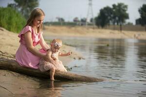 un hermosa madre es caminando con su pequeño hija por el río. maternidad. foto