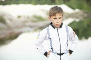 A handsome boy in a white suit of an American astronaut looks into the camera against the background of nature. photo