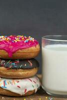 Lovely sweet food. Stack of glazed colorful assorted donuts with a cup of milk on a gray background. photo
