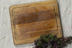 Cutting wood board and bunch of green basil on gray background photo