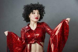 Vintage woman in afro wig and red disco costume on a gray background. Girl in the style of the seventies. photo