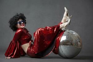 Woman in a wig with a disco ball on a gray background.Girl in disco style on a gray background. photo