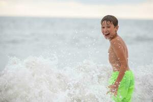 Happy boy bathes in the sea, plays with waves and splashes. photo