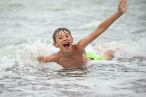 Happy boy playing with the sea wave, enjoying the sea. The child bathes, sunbathes and rests. Summer holidays. photo