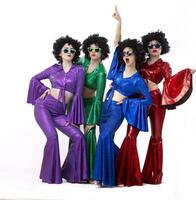 A group of girls in colorful flared suits and afro wigs pose against a white background. Disco style from the eighties or seventies. photo