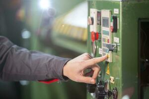 A worker's hand presses a button on a CNC machine. photo