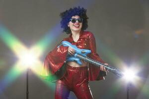 Cheerful woman in a red disco style stage costume holds a comic guitar in her hands. photo