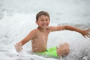contento chico jugando con el mar ola, disfrutando el mar. el niño se baña, toma el sol y descansa verano vacaciones. foto