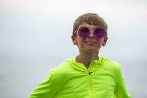 A handsome boy in a bright green sweater and purple sunglasses. Portrait of a happy ten year old boy. photo