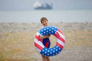 A happy boy wearing swimming goggles and an inflatable life buoy with the American flag painted on it. photo