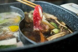 Raw beef slice on wood chopsticks for Japanese sukiyaki or hot pot photo