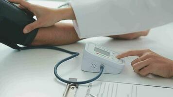 Female doctor checking old woman blood pressure at clinic and filling patient history in the morning. video