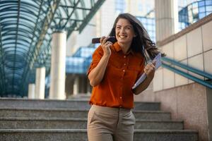 Smiling young business woman wearing suit standing on urban escalator using applications on cell phone, reading news on smartphone, fast connection, checking mobile apps outdoors. photo