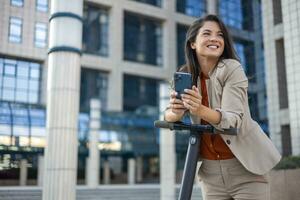 Female entrepreneur with smartphone while driving an electrical push scooter near business center on city street. Transportation environmental concept photo