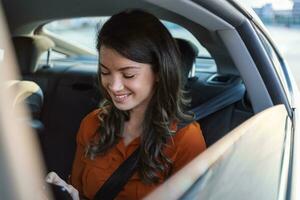 Beautiful business woman is using a smart phone and smiling while sitting on back seat in the car. Woman using a smart phone and smiling while sitting on the back seat of the car. photo