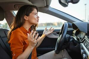 Portrait displeased angry pissed off aggressive woman driving car, shouting at someone in traffic hand fist up in air front windshield view. Emotional intelligence concept. Negative human expression photo