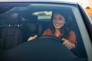 Beautiful young woman driving her new car at sunset. Woman in car. Close up portrait of pleasant looking female with glad positive expression, woman in casual wear driving a car photo