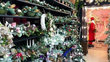 Christmas decorations in the store and Santa Claus standing at the door and greeting visitors. Decorative compositions of Christmas tree branches on the shelf and decorations on the market. video